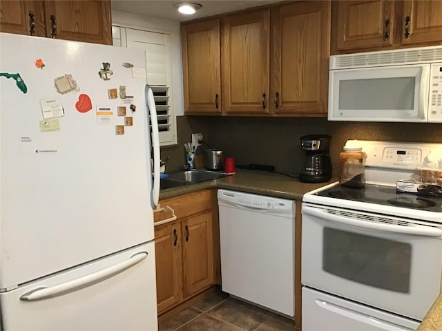 kitchen with dark tile patterned flooring, white appliances, dark countertops, and brown cabinets