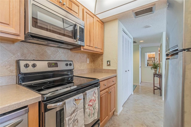 kitchen with light tile patterned floors, stainless steel appliances, tasteful backsplash, light brown cabinetry, and a textured ceiling