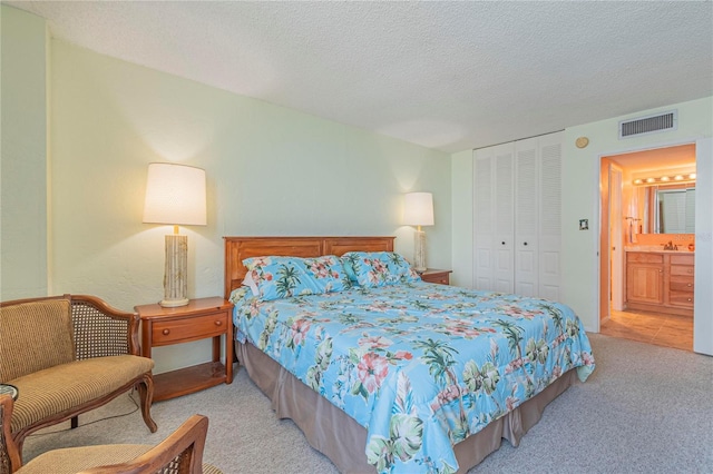 carpeted bedroom with ensuite bathroom, a closet, sink, and a textured ceiling