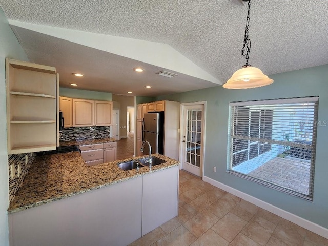 kitchen with hanging light fixtures, stainless steel fridge, sink, a textured ceiling, and tasteful backsplash