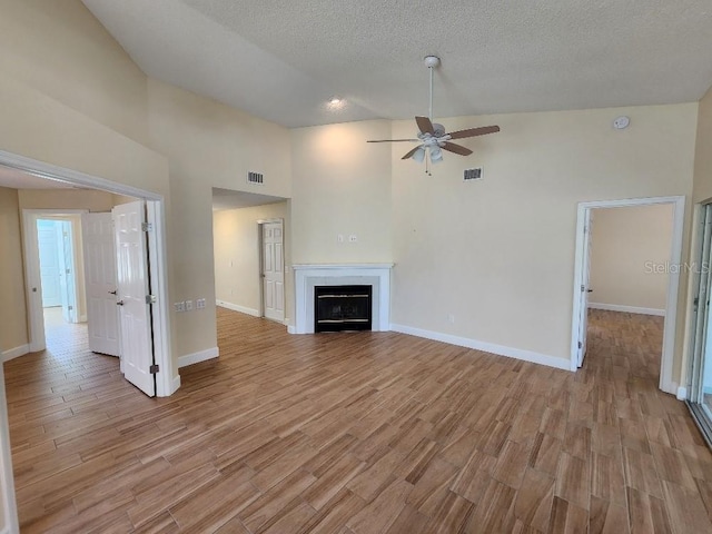 unfurnished living room with a textured ceiling, ceiling fan, high vaulted ceiling, and light wood-type flooring