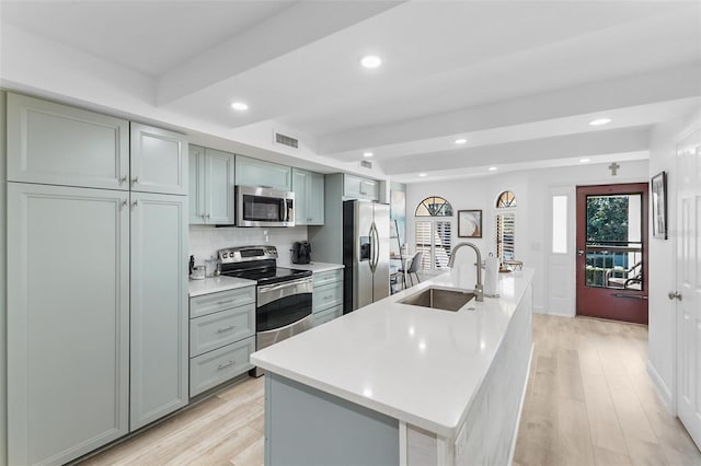 kitchen with sink, appliances with stainless steel finishes, backsplash, an island with sink, and light wood-type flooring