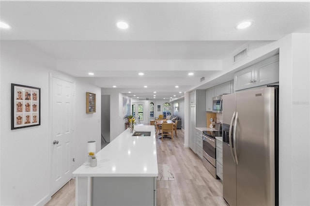 kitchen featuring sink, a center island, appliances with stainless steel finishes, gray cabinets, and light hardwood / wood-style floors