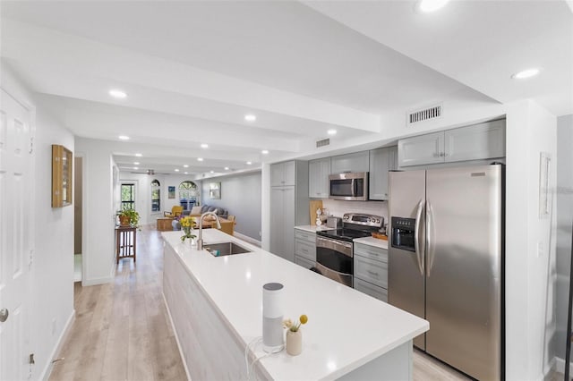 kitchen featuring sink, a kitchen island with sink, gray cabinets, stainless steel appliances, and light hardwood / wood-style floors