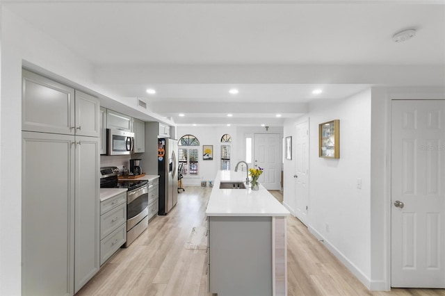 kitchen featuring a kitchen island with sink, sink, gray cabinets, and stainless steel appliances