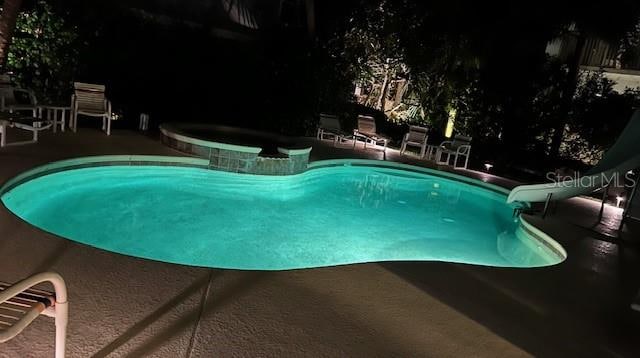pool at night featuring a patio, an in ground hot tub, and a water slide