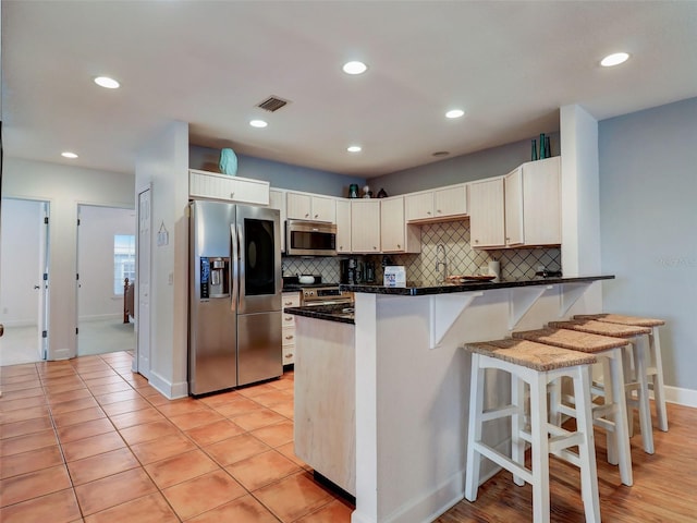 kitchen with stainless steel appliances, a kitchen bar, kitchen peninsula, tasteful backsplash, and dark stone countertops