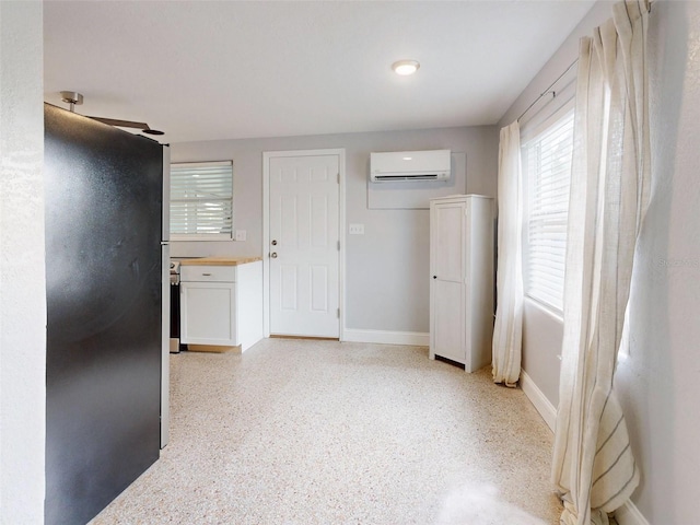 interior space featuring a wall unit AC, white cabinets, and black fridge