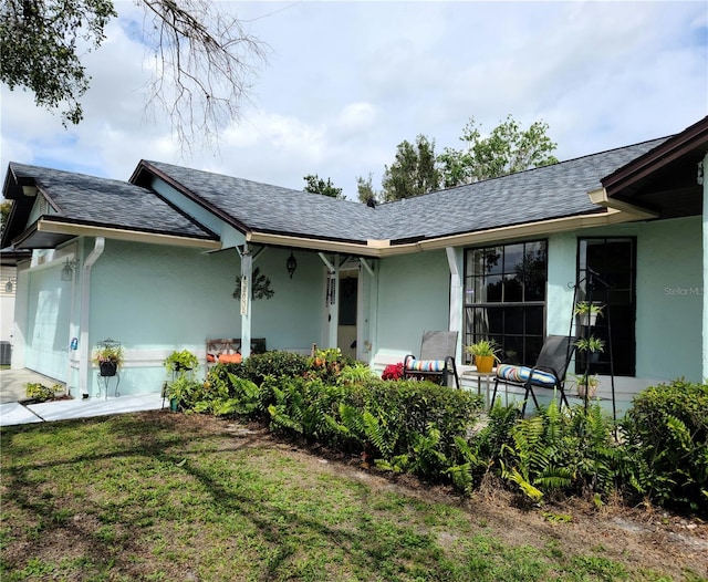 exterior space with a yard, roof with shingles, and stucco siding