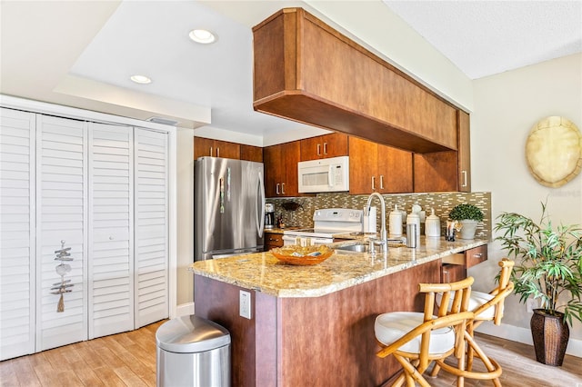 kitchen featuring kitchen peninsula, light stone countertops, backsplash, white appliances, and light hardwood / wood-style floors