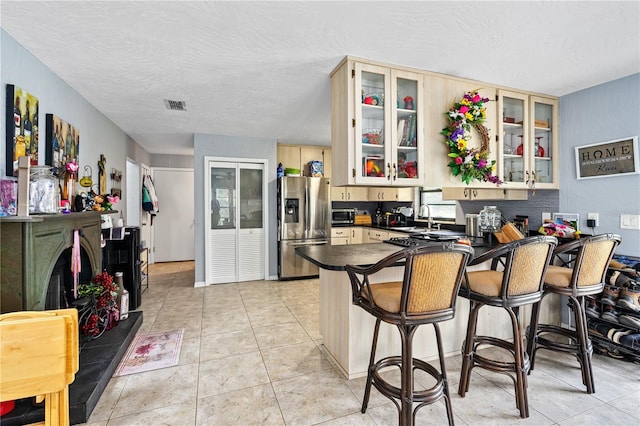 kitchen with a kitchen breakfast bar, kitchen peninsula, a textured ceiling, light tile patterned flooring, and appliances with stainless steel finishes