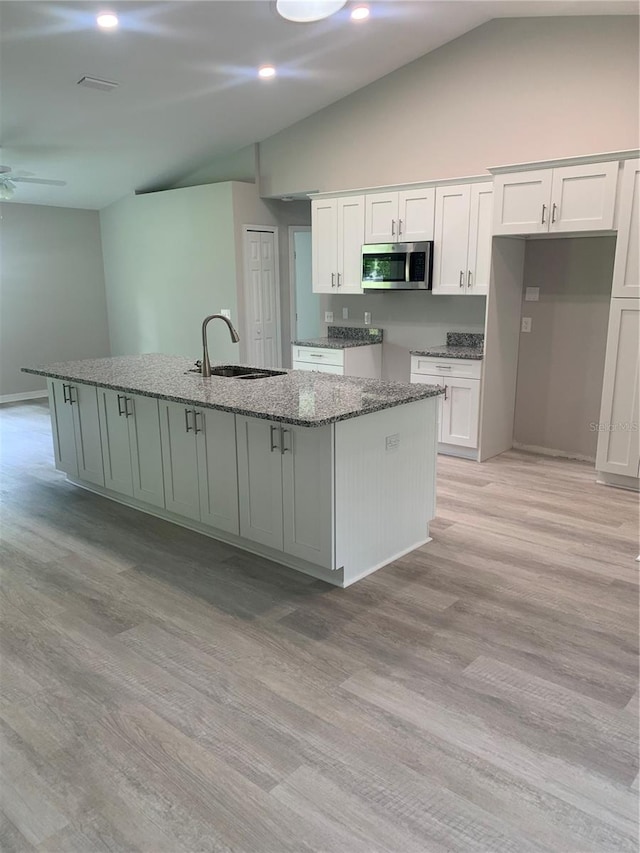 kitchen featuring vaulted ceiling, light hardwood / wood-style flooring, a kitchen island with sink, and white cabinetry