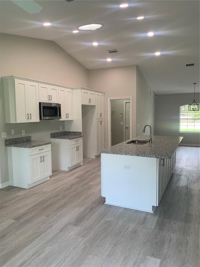 kitchen with a center island with sink, light hardwood / wood-style flooring, white cabinets, sink, and vaulted ceiling