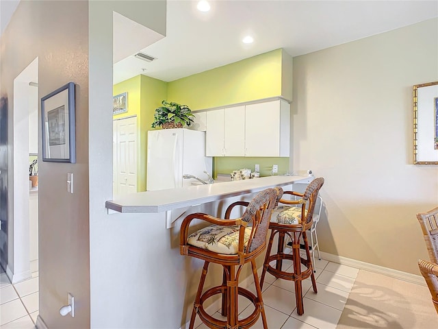 kitchen with kitchen peninsula, white cabinetry, light tile patterned flooring, and white refrigerator