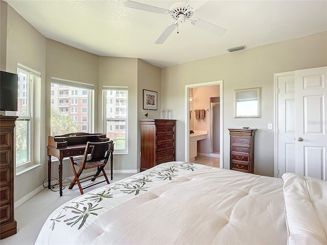 bedroom with connected bathroom, multiple windows, light colored carpet, and ceiling fan