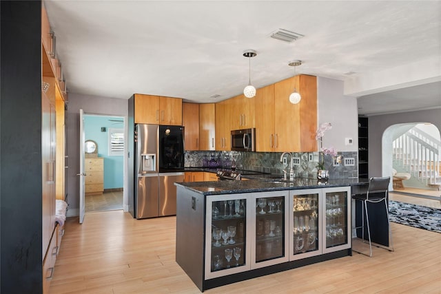 kitchen featuring appliances with stainless steel finishes, kitchen peninsula, decorative light fixtures, and light hardwood / wood-style flooring