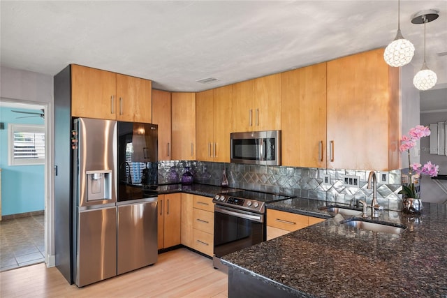 kitchen featuring sink, light hardwood / wood-style floors, stainless steel appliances, decorative light fixtures, and dark stone countertops