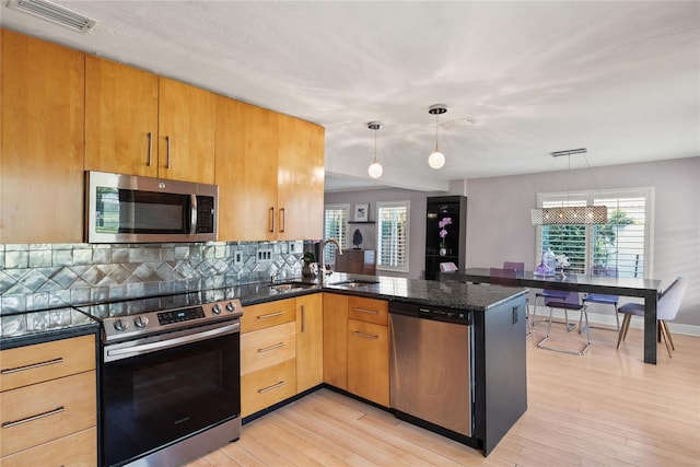 kitchen with hanging light fixtures, stainless steel appliances, light hardwood / wood-style floors, and dark stone countertops