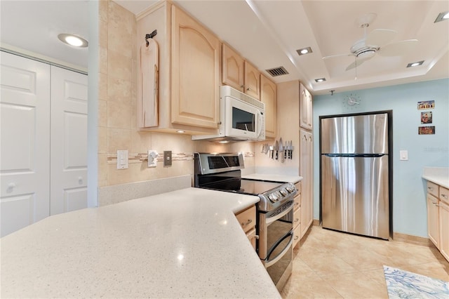 kitchen featuring ceiling fan, light brown cabinets, light tile patterned floors, appliances with stainless steel finishes, and a tray ceiling