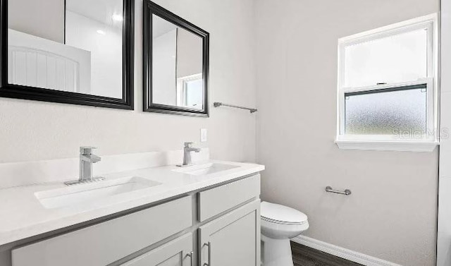 bathroom with wood-type flooring, large vanity, toilet, and dual sinks