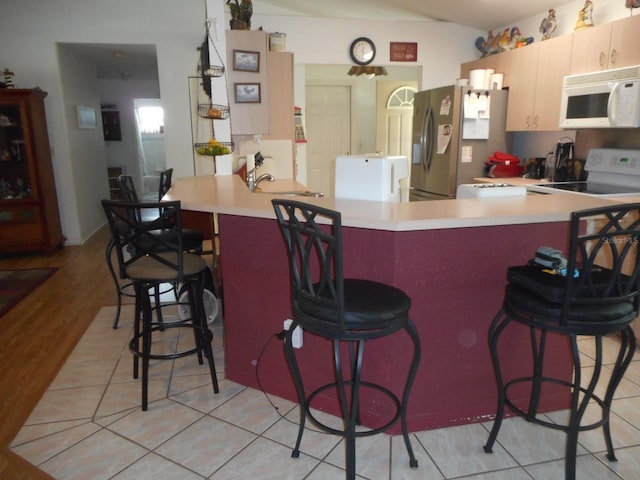 kitchen featuring a breakfast bar area, light wood-type flooring, kitchen peninsula, stainless steel fridge, and stove