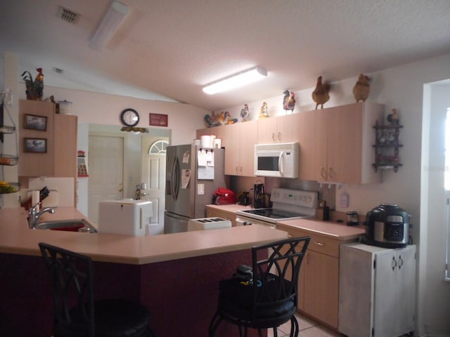 kitchen featuring white appliances, sink, kitchen peninsula, lofted ceiling, and a kitchen breakfast bar