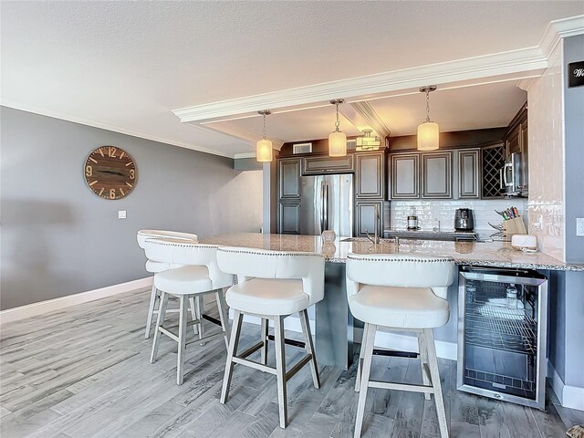 kitchen with wine cooler, stainless steel refrigerator, decorative light fixtures, and light stone countertops