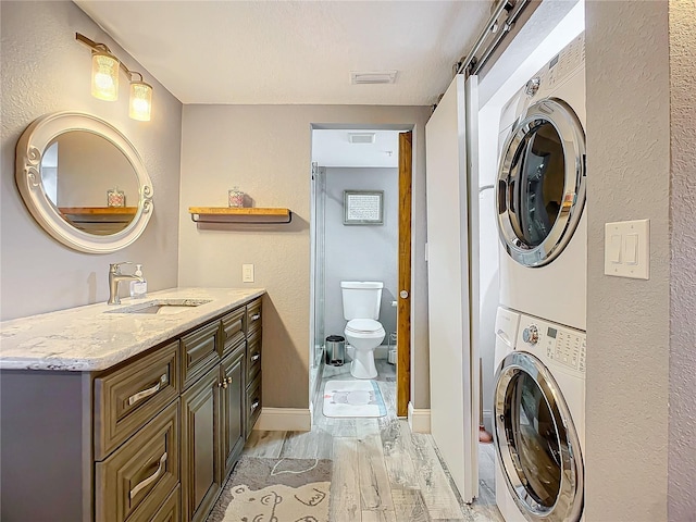 washroom with sink, stacked washer and clothes dryer, and light hardwood / wood-style floors