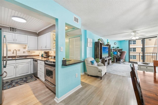 kitchen with appliances with stainless steel finishes, light wood-type flooring, ceiling fan, sink, and white cabinets