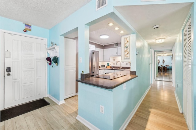 kitchen featuring stainless steel fridge, white cabinetry, kitchen peninsula, and light wood-type flooring