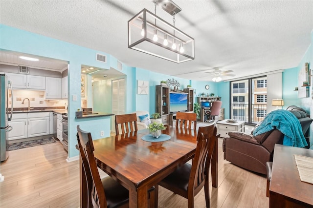 dining room featuring ceiling fan, light hardwood / wood-style floors, sink, and a textured ceiling