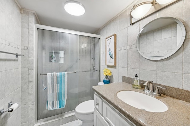 bathroom with vanity, toilet, a shower with door, and tile walls