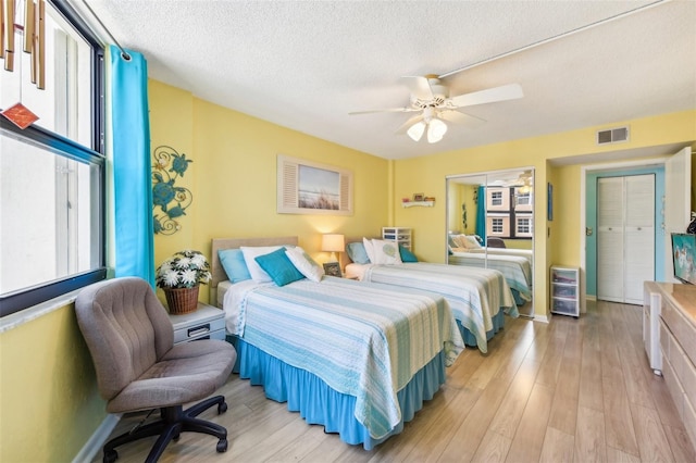 bedroom featuring light wood-type flooring, a textured ceiling, ceiling fan, beverage cooler, and a closet