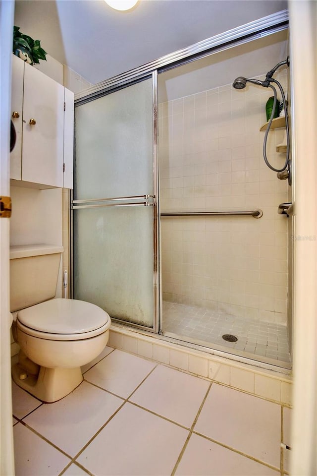 bathroom featuring tile flooring, toilet, and a shower with shower door