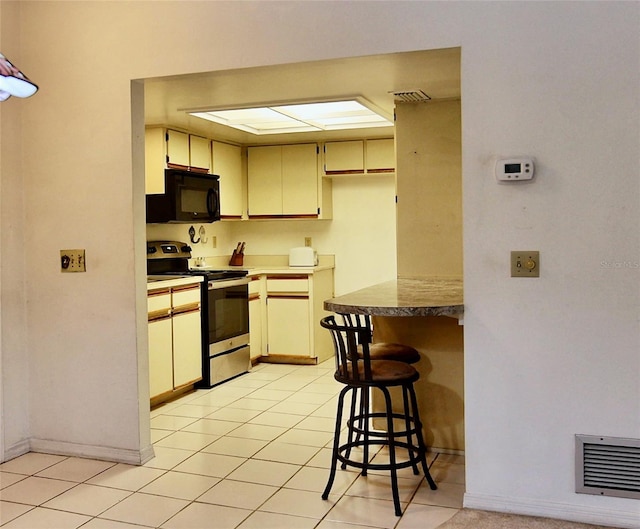 kitchen with visible vents, electric stove, cream cabinets, light countertops, and black microwave