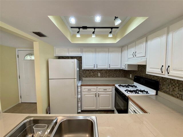 kitchen featuring white refrigerator, a tray ceiling, gas range oven, and white cabinets