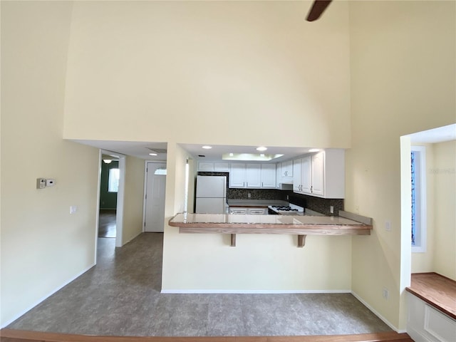 kitchen with white cabinetry, white refrigerator, a kitchen breakfast bar, kitchen peninsula, and backsplash