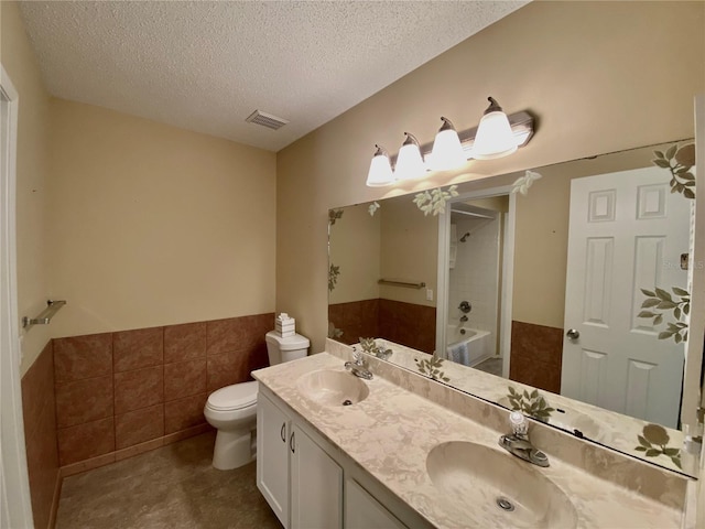 full bathroom featuring tile walls, vanity, toilet, tub / shower combination, and a textured ceiling