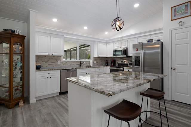 kitchen featuring a kitchen island, stainless steel appliances, vaulted ceiling, light wood-type flooring, and white cabinetry