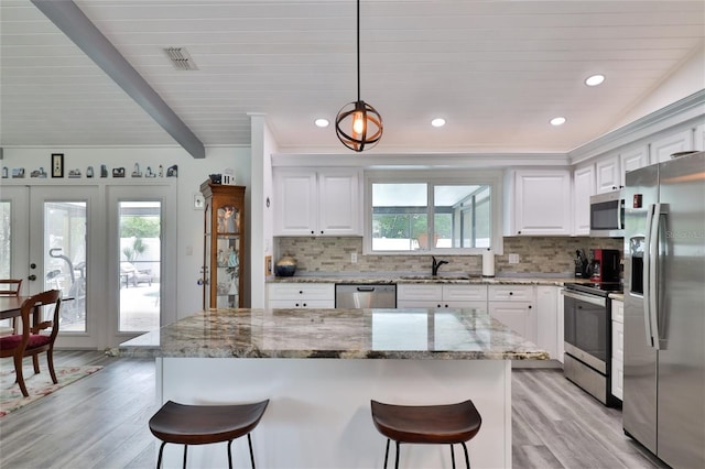 kitchen featuring white cabinets, light stone counters, appliances with stainless steel finishes, light hardwood / wood-style floors, and decorative light fixtures