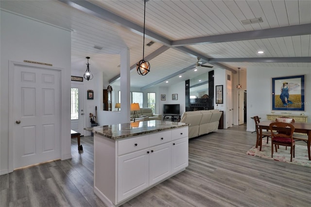 kitchen featuring white cabinetry, hardwood / wood-style flooring, dark stone counters, lofted ceiling with beams, and decorative light fixtures