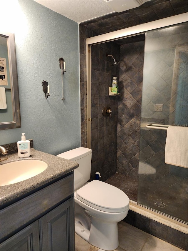 bathroom with a shower with shower door, vanity, toilet, and tile floors