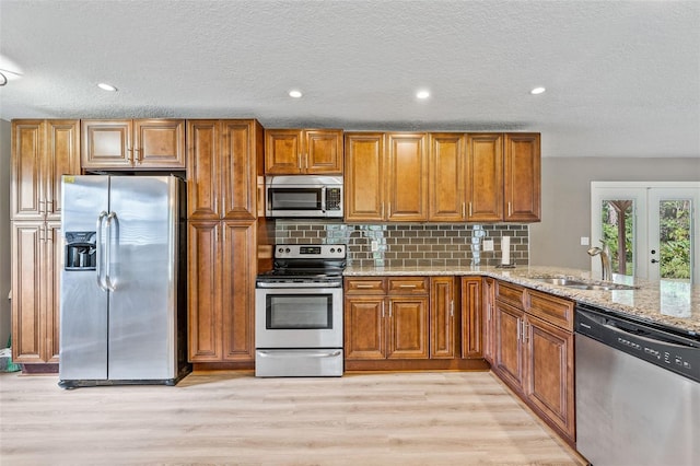 kitchen with appliances with stainless steel finishes, a textured ceiling, light stone countertops, sink, and light hardwood / wood-style floors