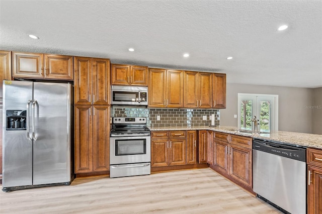 kitchen featuring light hardwood / wood-style floors, sink, backsplash, light stone countertops, and appliances with stainless steel finishes