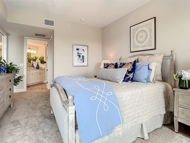 bedroom with ensuite bathroom and light colored carpet