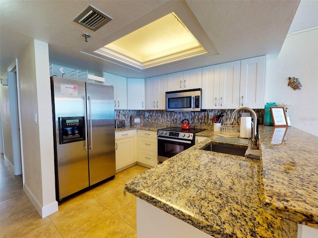 kitchen featuring appliances with stainless steel finishes, a tray ceiling, white cabinets, backsplash, and sink