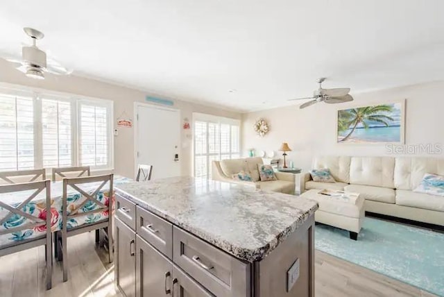 kitchen with ceiling fan, a center island, light stone countertops, and light wood-type flooring