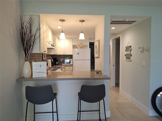 kitchen with white cabinetry, kitchen peninsula, a kitchen breakfast bar, white appliances, and decorative light fixtures