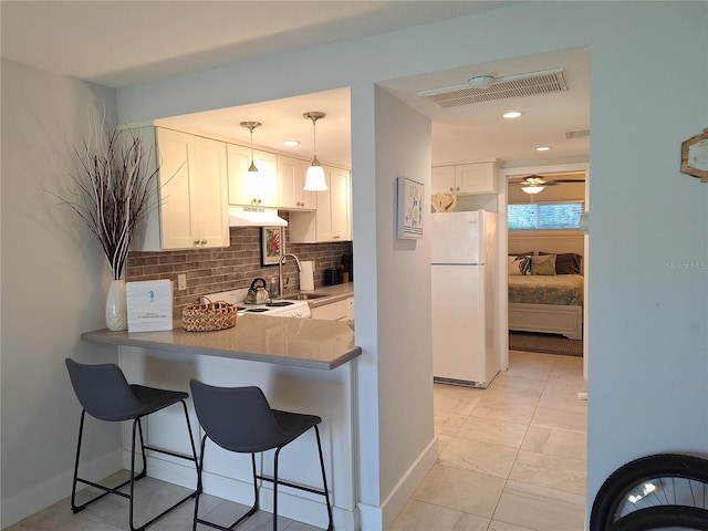 kitchen featuring hanging light fixtures, a kitchen breakfast bar, white refrigerator, white cabinets, and kitchen peninsula