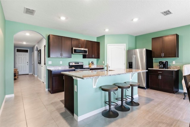 kitchen featuring a kitchen island with sink, sink, dark brown cabinets, and appliances with stainless steel finishes